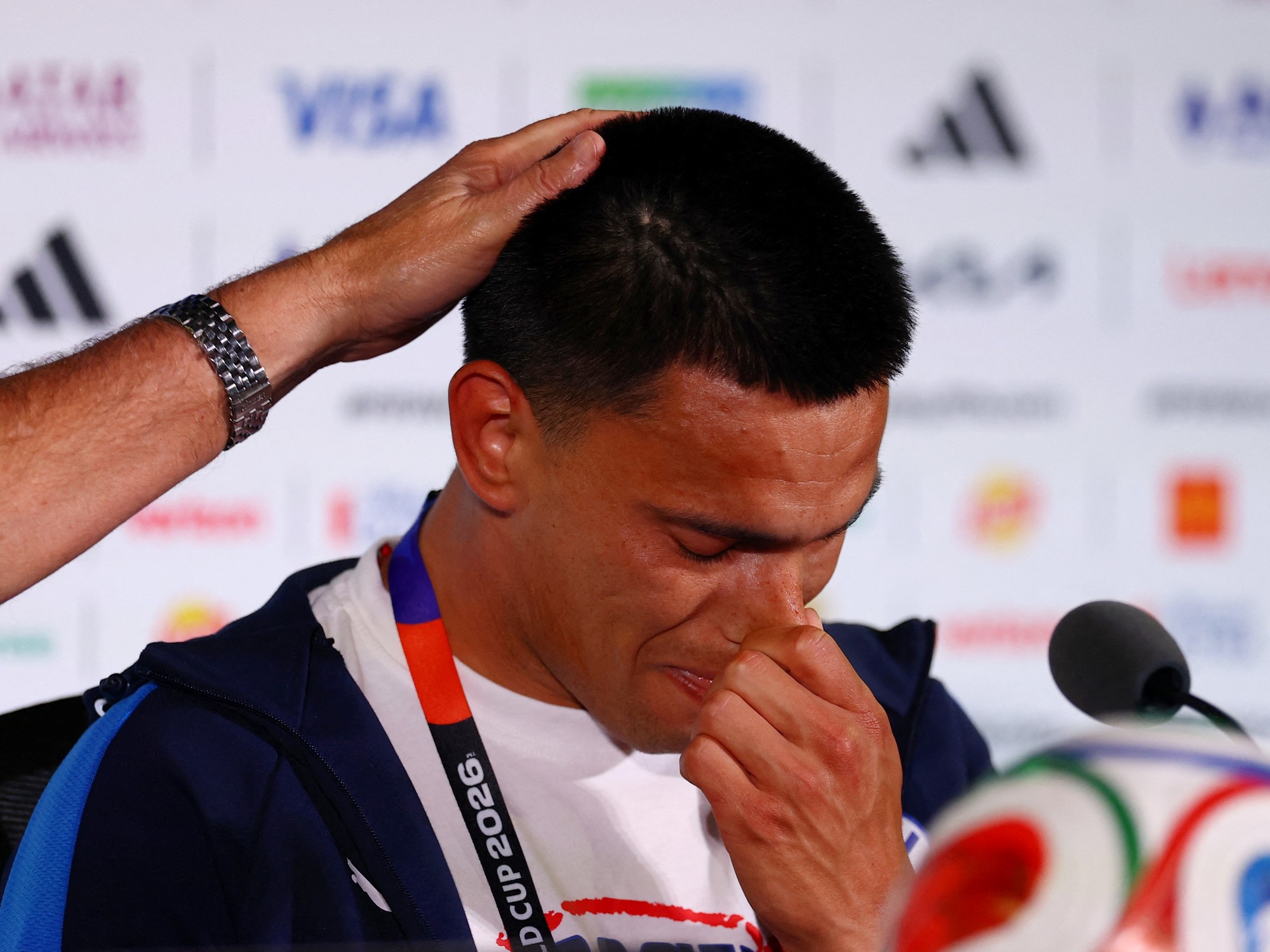 El futbolista Diego Gómez, visiblemente emocionado, es consolado por el técnico Gustavo Alfaro en una rueda de prensa previa al Mundial.